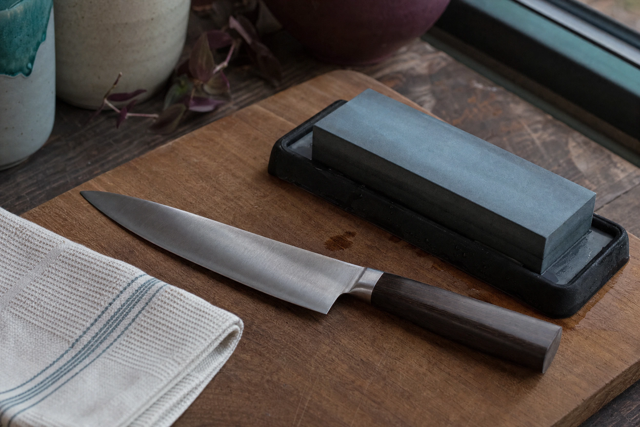 A chef knife and whetstone on a kitchen worktop.